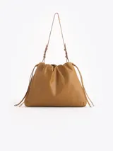 Cartera tipo shopper de cuero vacuno color tostado, con formato amplio, fruncido superior y cordones ajustables a los lados. Cuenta con tiras finas para llevar al hombro y sutil grabado de la marca en el frente.