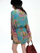 Kimono de corte amplio con mangas anchas, confeccionado en tela con mezcla de estampados florales y geométricos en tonos azules, rosados y dorados. Incluye un cinturón fino del mismo tejido para ajustar a la cintura.