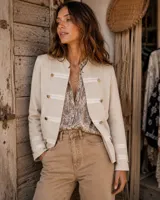 Chaqueta de algodón color beige de estilo militar, con cuello mao, detalles de bandas horizontales en tono más claro y botones dorados decorativos en el frente y puños.