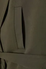 Chaleco de cuello solapa y escote pico cruzado, con hombreras y manga sisa. Presenta bolsillos de vivo en el delantero, forro interior y cierre frontal cruzado con botones. Incluye un cinturón de lazada en el mismo tejido.