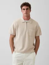 Buzo tipo polo de manga corta en color beige, confeccionado en tejido de punto, con cierre frontal parcial de cremallera y un bolsillo aplicado en el pecho.