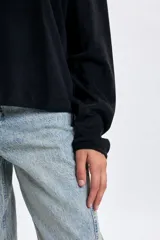 Buzo de polar negro con cuello alto y cierre frontal parcial. Presenta un diseño de corte holgado con mangas largas y costuras horizontales en el pecho.
