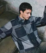 Campera de jacquard con diseño patchwork cuadriculado en tonos de azul. Presenta cuello inglés, cierre frontal con botones metálicos y bolsillos delanteros.