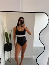 Traje de baño entero negro con banda horizontal blanca a la altura del busto.