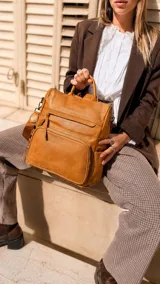 Mochila de símil cuero color marrón, con apertura superior, dos bolsillos frontales con cierre metálico y bolsillos laterales. Incluye tres bolsillos internos y correa extraíble.