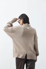 Polera de tejido de punto color gris, con cuello alto, mangas largas abullonadas con puños elásticos y costura central vertical en el frente. Presenta una abertura sutil en la espalda.