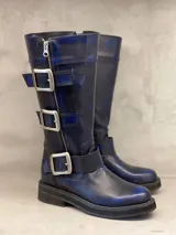 Bota de cuero azul de caña alta, con hebillas de metal y cierre lateral con cremallera. Suela de goma con plataforma. Hecha a mano en Uruguay.