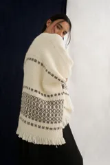Ruana tejida en lana con diseño de guardas geométricas en tonos crudo y marrón, con terminación de flecos en el ruedo.