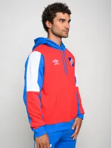 Canguro de felpa Umbro del Club Nacional de Football, con diseño tricolor en rojo, azul y blanco. Presenta capucha con cordones ajustables, bolsillo tipo canguro frontal, logo de la marca y escudo del club bordados en el pecho.
