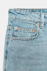 Jeans de tiro medio y corte bootcut cropped de Zara Woman Collection. Confeccionados en denim de efecto lavado en color celeste, presentan diseño de cinco bolsillos, trabillas para cinto, detalle de rotura en la rodilla izquierda y bajo evasé sin costuras. Cierre frontal con cremallera y botón metálico.