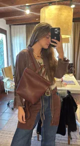Mochila de cuero marrón con diseño minimalista, silueta estructurada, asas superiores y correas ajustables para la espalda.