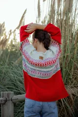 Sweater rojo de lana merino con cuello redondo y mangas largas. Presenta un canesú con diseño geométrico multicolor en tonos blanco, rojo, azul, verde y rosa.