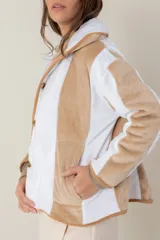 Campera de peluche con diseño de paneles verticales en colores blanco y beige. Presenta capucha, cierre frontal y puños de tejido elástico en tono contrastante.