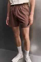 Short deportivo de entrenamiento en color marrón, confeccionado en tejido técnico ligero y elástico. Cuenta con cintura elástica ajustable con cordón, bolsillos frontales, bolsillo trasero con cierre y aberturas laterales en el bajo. Incluye un pequeño detalle de logo estampado en la pierna.