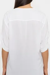 Blusa blanca de corte relajado, con escote en V y mangas largas con sistema de ajuste mediante trabilla y botón para llevarlas arremangadas. Confeccionada en tejido de viscosa con caída fluida y ruedo redondeado.