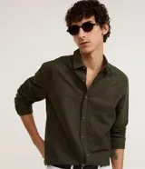 Camisa de algodón color verde militar, con cuello inglés, manga larga, cierre frontal con botones y textura maquinetada.