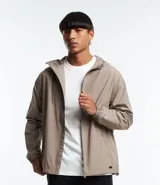 Campera rompevientos color beige con capucha y cordón ajustable, cierre frontal con cremallera, bolsillos laterales con cremallera y puños elásticos.