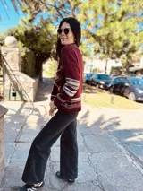 Sweater marrón de lana con cuello alto y manga larga. Presenta un copo de nieve blanco en el frente y bordados a mano. Tiene puños y cuello con diseño geométrico en tonos blanco, marrón y negro.