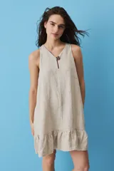 Vestido corto de lino color beige, de silueta suelta y sin mangas, con escote en V decorado con un botón, bolsillos laterales y detalle de volado en el ruedo.