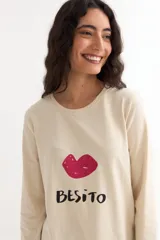 Remera de manga larga color beige con cuello redondo a la base. Presenta un estampado frontal con un dibujo de labios en color fucsia y la palabra 'BESITO' en color negro.