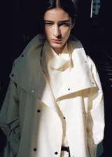 Chaqueta larga de algodón color crudo, diseño oversize con cuello embudo, cierre frontal cruzado con botones y mangas largas con trabillas en los puños.