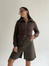 Sweater tipo campera de tejido de punto con diseño de trenzas, color blanco, con cuello alto y cierre frontal completo.