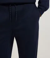 Pantalón jogger negro de algodón y poliéster, con cintura elástica y cordón ajustable. Presenta bolsillos laterales y puños ajustados en los tobillos.