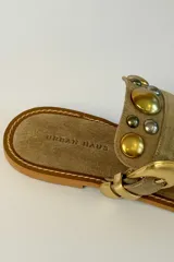Sandalia plana de gamuza marrón, estilo ojota, con apliques metálicos dorados y hebilla decorativa.