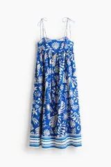 Vestido midi en mezcla de viscosa, de color azul con estampado botánico en tono blanco. Presenta breteles spaghetti con moños para atar, escote cuadrado, canesú ajustado con punto smock en la espalda y falda larga y fruncida con diseño de guardas en el ruedo.