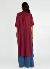 Camisa larga tipo vestido, de corte recto y diseño traslúcido, con cuello clásico, cierre frontal de botones y mangas cortas con dobladillo.