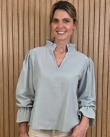 Blusa blanca de algodón con escote en V y cuello mao. Presenta mangas largas abullonadas con puños acampanados y fruncidos.