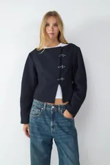 Campera corta de paño color negro, con escote redondo y manga larga. Presenta cierre frontal mediante tres ganchos metálicos decorativos. Diseño entallado con forro interior.