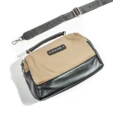 Bandolera de cuero sintético color beige con base en cuero sintético negro, con correa de tela negra con letras blancas y logo de la marca.