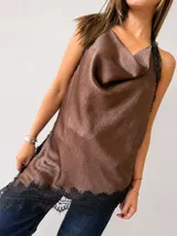 Blusa de inspiración lencera color marrón, con escote buche y detalles de encaje negro en los bordes. Presenta un diseño asimétrico con ruedo en pico y espalda descubierta.