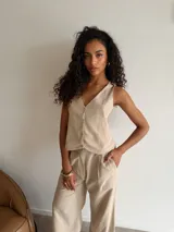 Chaleco de corte sastrero en tejido tusor color beige con sutiles rayas verticales. Presenta escote en V, cierre frontal con botones y diseño sin mangas.