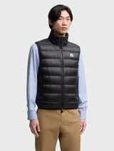 Chaleco puffer negro con diseño acolchado de costuras horizontales, cuello alto y cierre frontal de cremallera. Incluye el parche del logo de Moncler en el pecho.