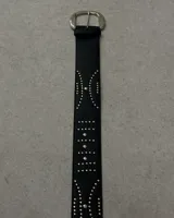 Cinturón negro de cuero sintético con hebilla metálica plateada estilo western y apliques de tachas plateadas.