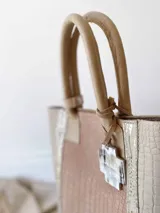 Bolso matero de cuero color beige y nude con textura croco. Tiene doble asa de mano color cuero y dije colgante con forma de cruz. No tiene división interna y se le puede agregar una correa larga opcional.