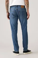 Pantalón de jean corte slim taper, con diseño de cinco bolsillos, cierre de cremallera y botón metálico, en tono azul medio con efecto lavado.