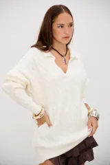 Sweater de punto grueso color crudo, con cuello polo y escote en V. Presenta un diseño de trenzas en toda la prenda y es de corte holgado.