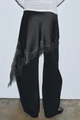 Falda corta de tiro medio confeccionada en tejido satinado negro, con bajo asimétrico y aplicación de encaje a tono.