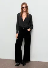 Pantalón de terciopelo negro de tiro medio y diseño wide leg con cinco bolsillos, cierre de botón y cremallera, y trabillas para cinturón.