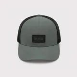 Gorro trucker gris con parte posterior de malla negra, visera curva y parche frontal con el logo de la marca.