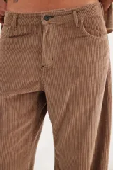 Pantalón de pana de corte ancho y tiro medio-bajo, con diseño de cinco bolsillos y acabado lavado. Presenta un aplique cuadrado decorativo en una de las piernas y un pin bordado de la marca.