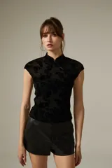 Top negro de corte ajustado con cuello mao y cierre frontal con botones. Presenta un diseño de encaje con patrón floral sutil y mangas cortas.