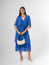 Vestido midi de seda italiana color azul, con escote en V, mangas murciélago amplias, falda de tres volados y cintura elastizada con lazo ajustable al tono y hebilla circular dorada.