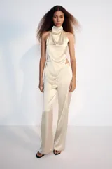 Pantalón flare de tiro alto confeccionado en tejido satinado color negro, con bajo en línea evasé y cierre frontal con cremallera oculta y gancho metálico.