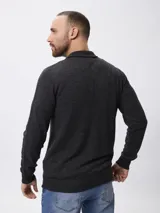 Campera tejida de punto con cierre frontal completo, cuello alto y mangas largas. Presenta un diseño liso en color gris oscuro con detalles en el cierre.