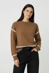 Sweater de tejido de punto color marrón con detalles de líneas horizontales en color blanco en las mangas y el ruedo. Presenta cuello redondo a la base, mangas largas y un corte holgado.