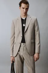 Blazer slim fit de color beige, confeccionada en tejido con lana. Presenta cuello con solapas de muesca, cierre frontal de un botón, bolsillos laterales con solapa y bolsillo de vivo en el pecho.